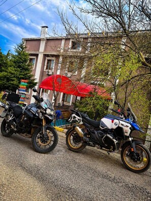 Zwei Motorräder sind auf einer Straße geparkt, im Hintergrund sind Gebäude und ein roter Regenschirm zu sehen.