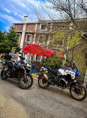 Två motorcyklar står parkerade på en gata med byggnader, och i bakgrunden syns ett rött parasoll.