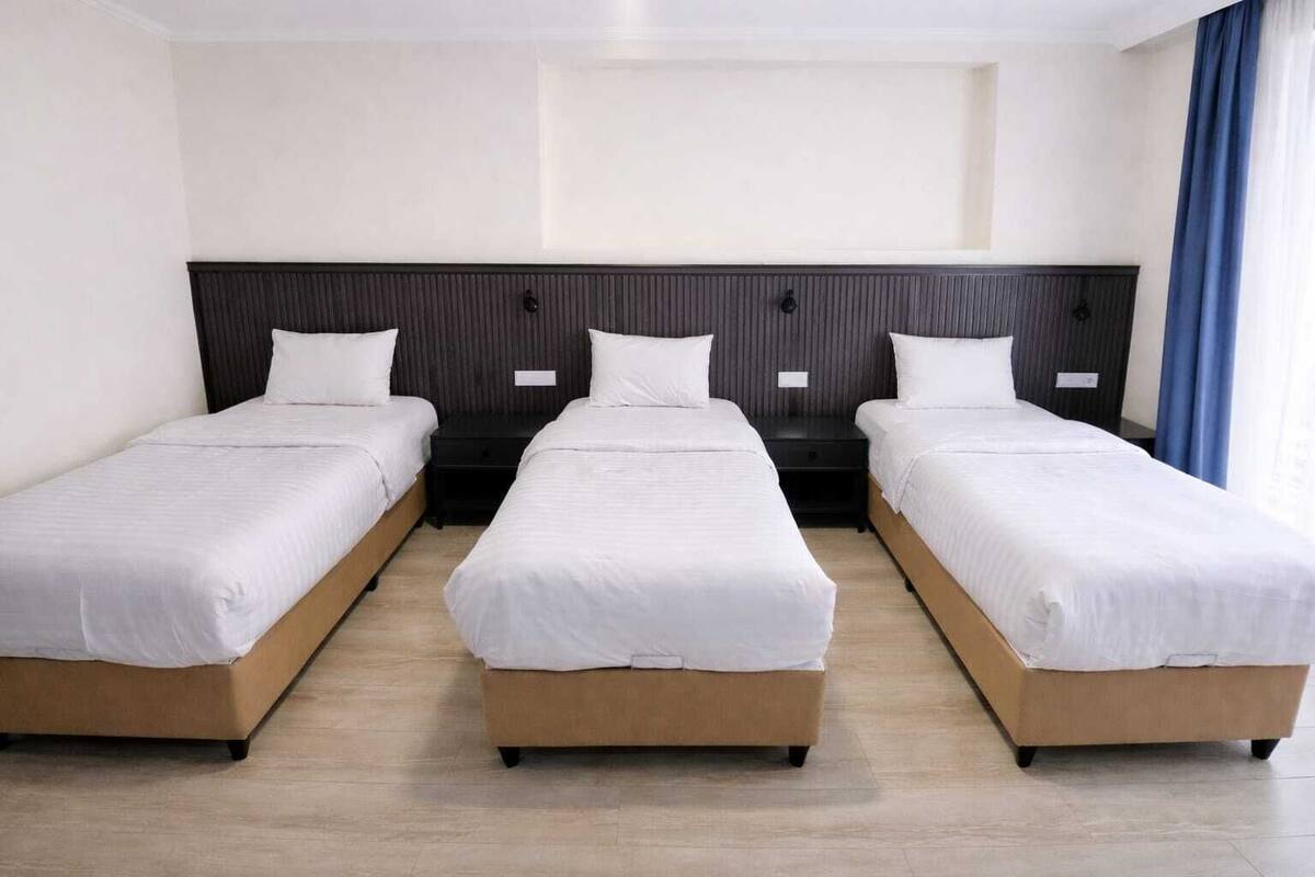 Ett hotellrum med tre separata sängar, trägavlar och ett ljust golv.