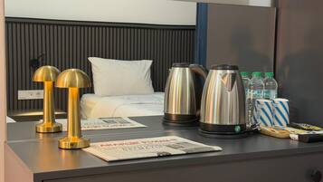 Una habitación de hotel con cama, lámparas de noche, periódico, tetera y agua embotellada.