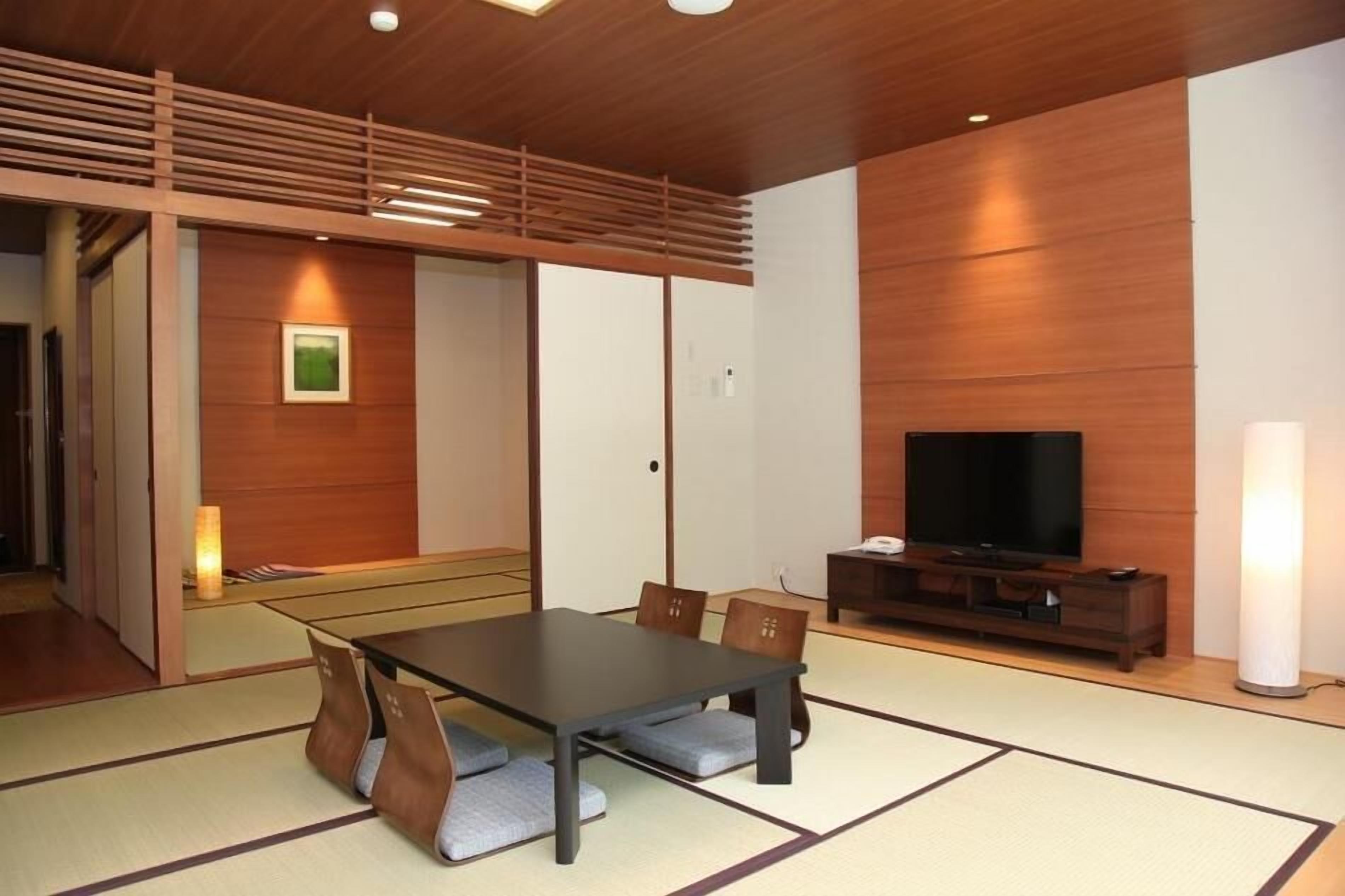 A modern room with tatami flooring, a wooden ceiling, a TV, and a traditional Japanese-style table with cushions.