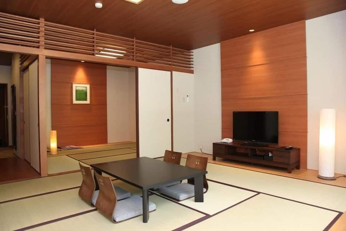 Quarto moderno com piso de tatame, teto de madeira, televisão e mesa tradicional japonesa com almofadas.