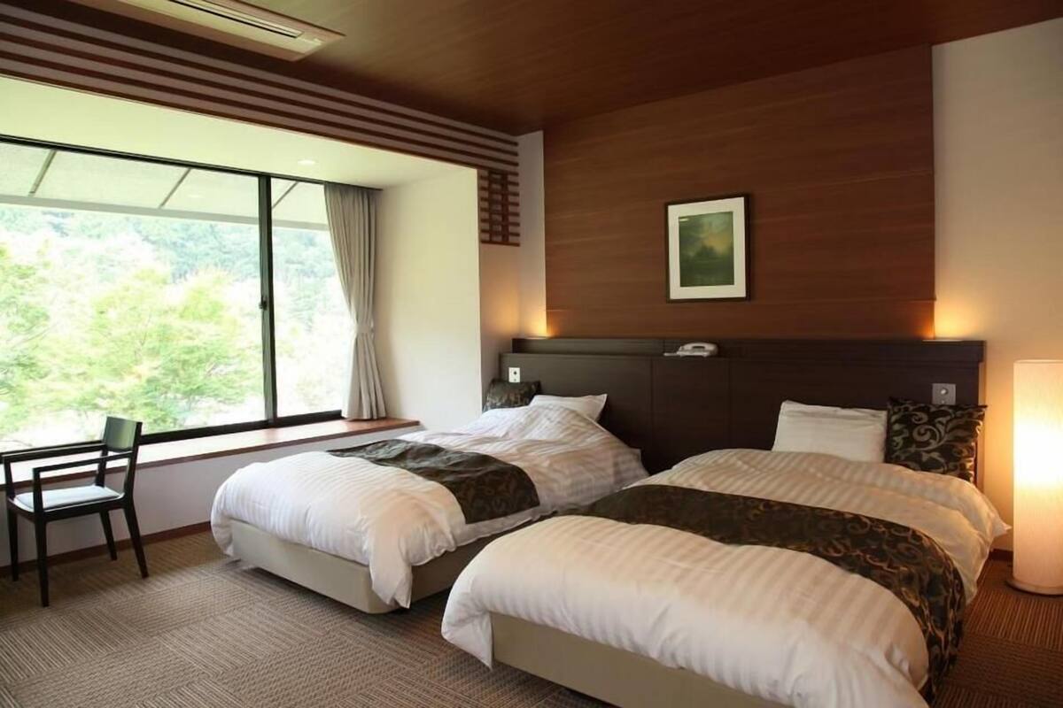 Quarto de hotel com duas camas, uma escrivaninha e uma cadeira.