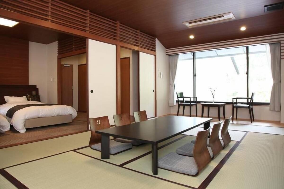 Quarto de hotel com cama, mesa de jantar, cadeiras, tatames e uma porta deslizante.