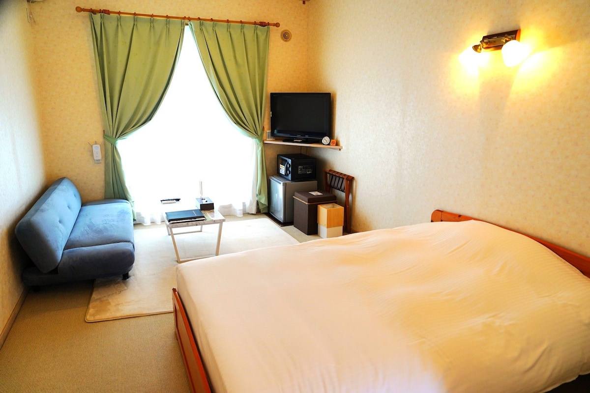 A hotel room with a bed, a sofa, a television, a small table, and a desk with a computer.