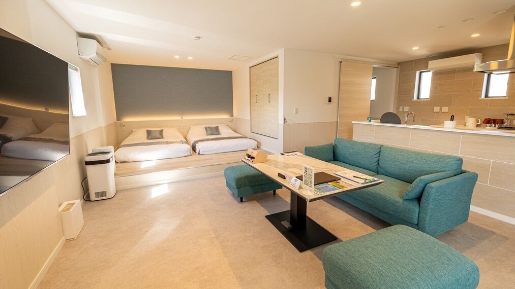 A modern hotel room with a sofa, a small table, a bed, and a kitchenette.