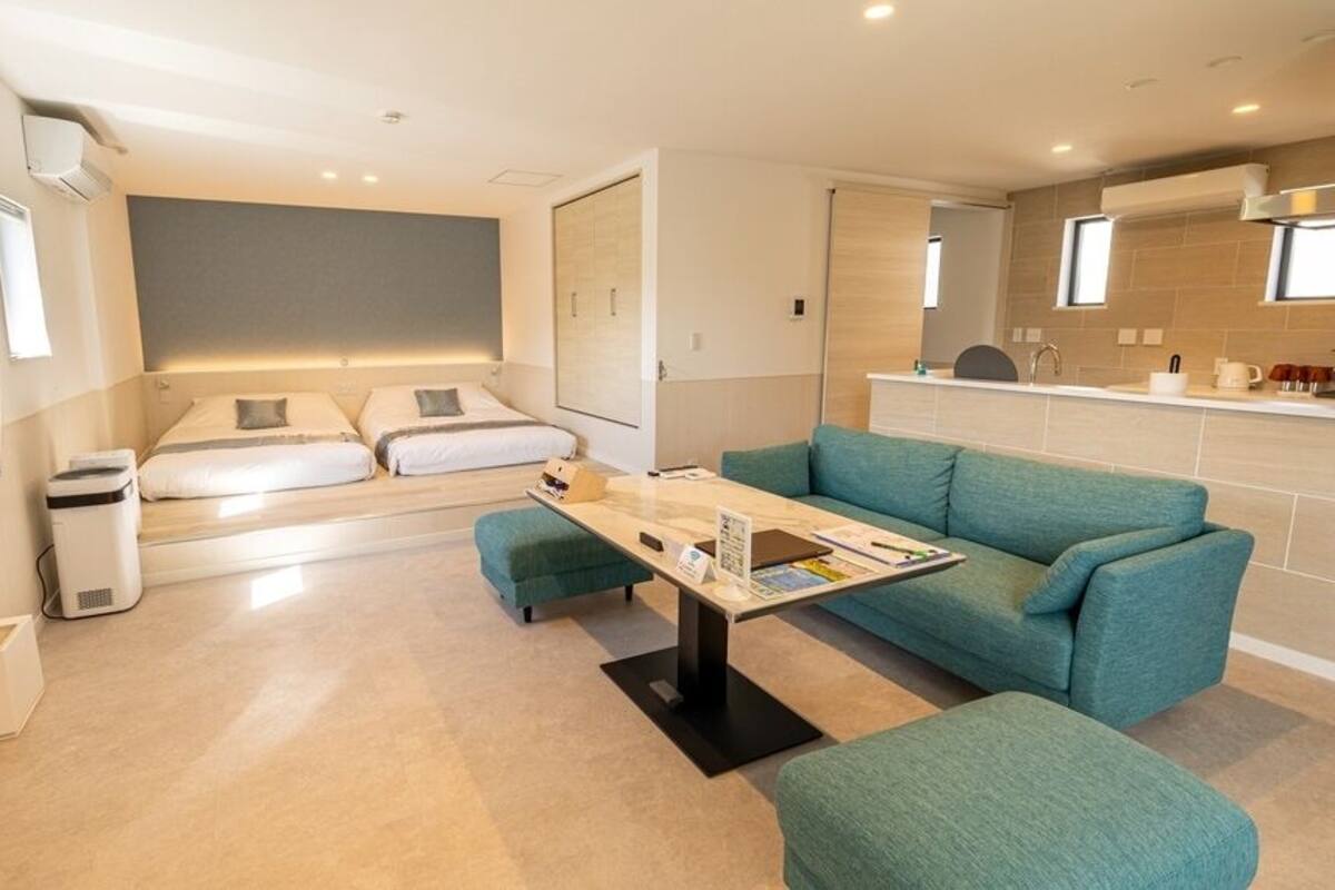 A modern hotel room with a sofa, a small table, a bed, and a kitchenette.