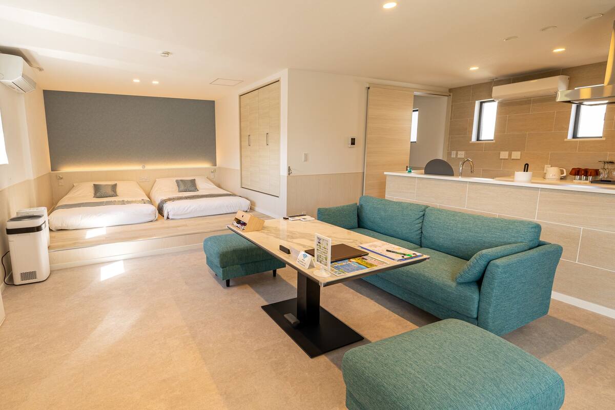 A modern hotel room with a sofa, a small table, a bed, and a kitchenette.