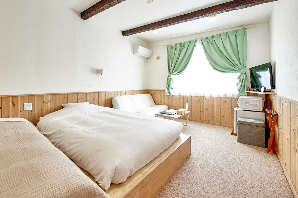 Una camera da letto con testiera in legno, un letto con biancheria bianca, un comodino, una TV e una finestra con tende verdi.