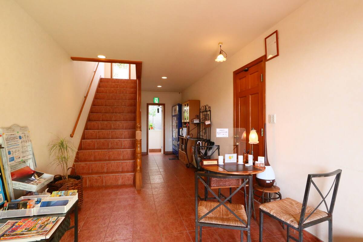 A hotel lobby with a staircase, a reception desk, and a dining area with chairs and a table.