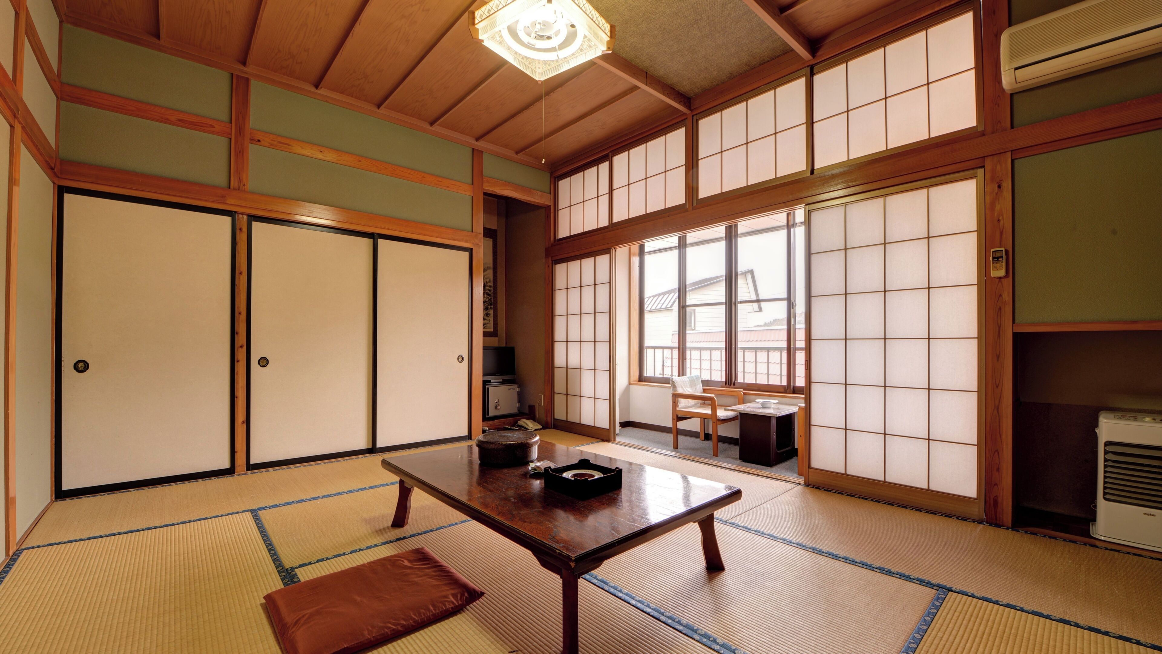 A traditional Japanese room with tatami flooring, sliding doors, a wooden table, and a view through large windows.