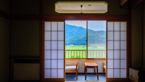 A traditional Japanese room with tatami flooring, a sliding shoji door, a small table, and a view of a green landscape with mountains.