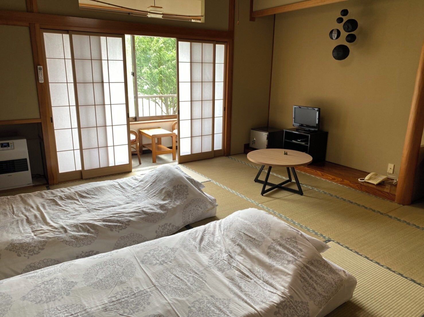 Une pièce de style japonais traditionnel, avec un sol recouvert de tatamis, deux futons posés sur des tatamis, une petite table ronde, un téléviseur et une porte coulissante donnant sur un balcon.