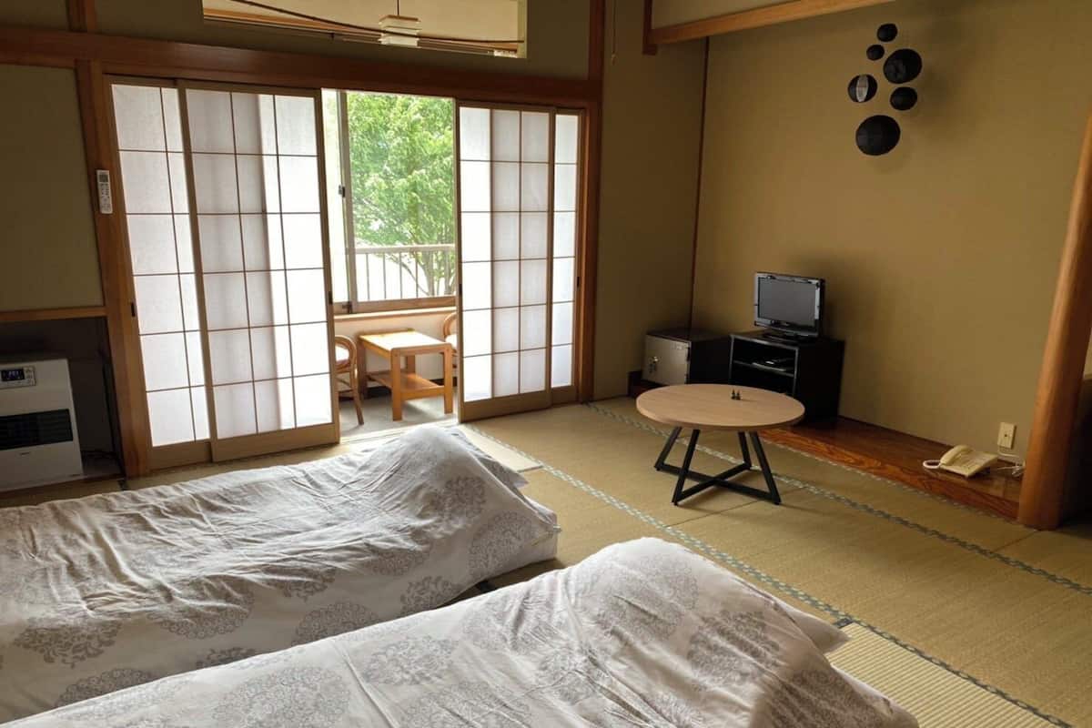 Une pièce de style japonais traditionnel, avec un sol recouvert de tatamis, deux futons posés sur des tatamis, une petite table ronde, un téléviseur et une porte coulissante donnant sur un balcon.