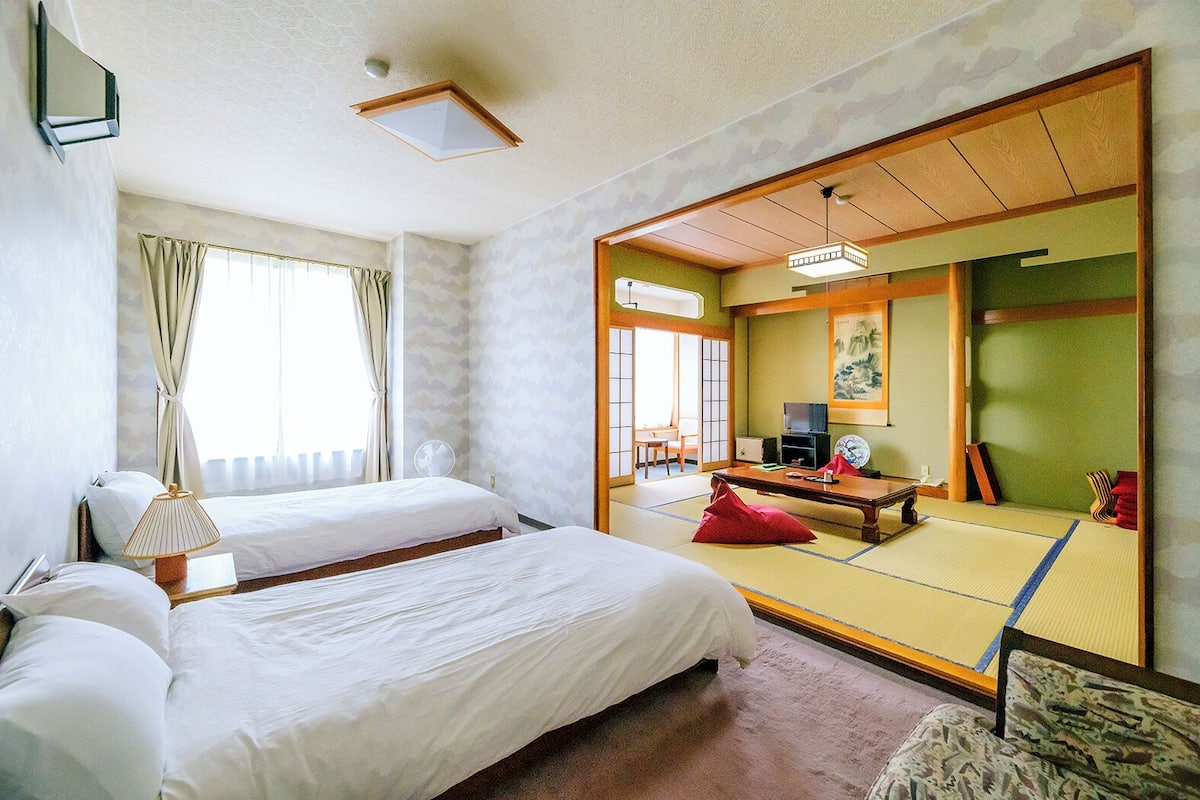 Une chambre d’hôtel avec deux lits, un bureau, une chaise, une télévision et une porte coulissante de style japonais traditionnel.