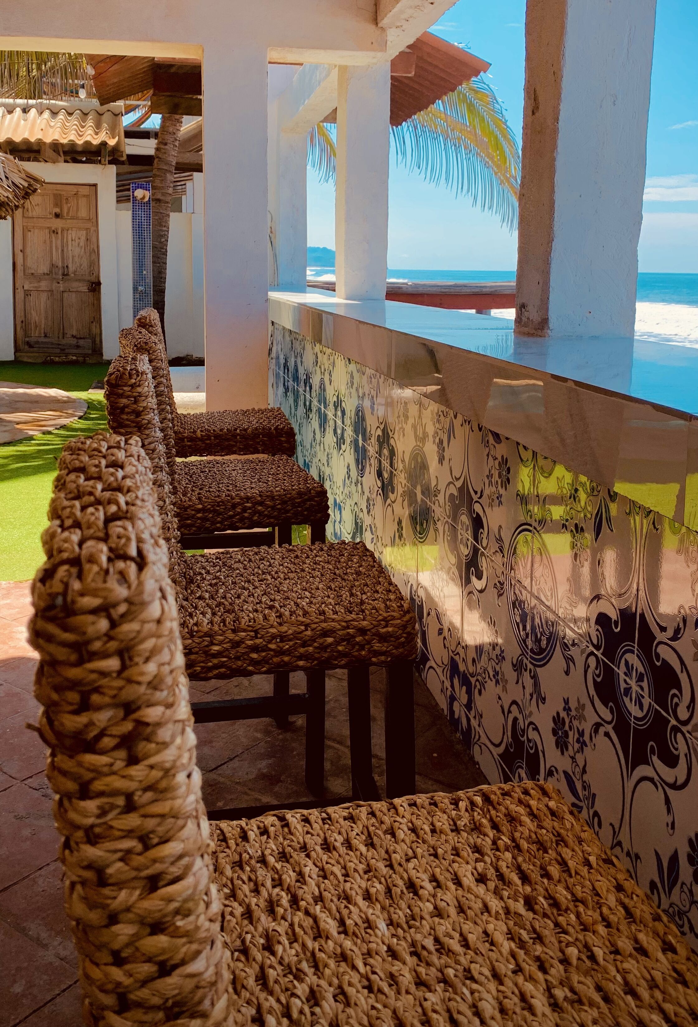 Un espace bar situé au bord de la plage, avec des chaises en osier et une vue sur l’océan.