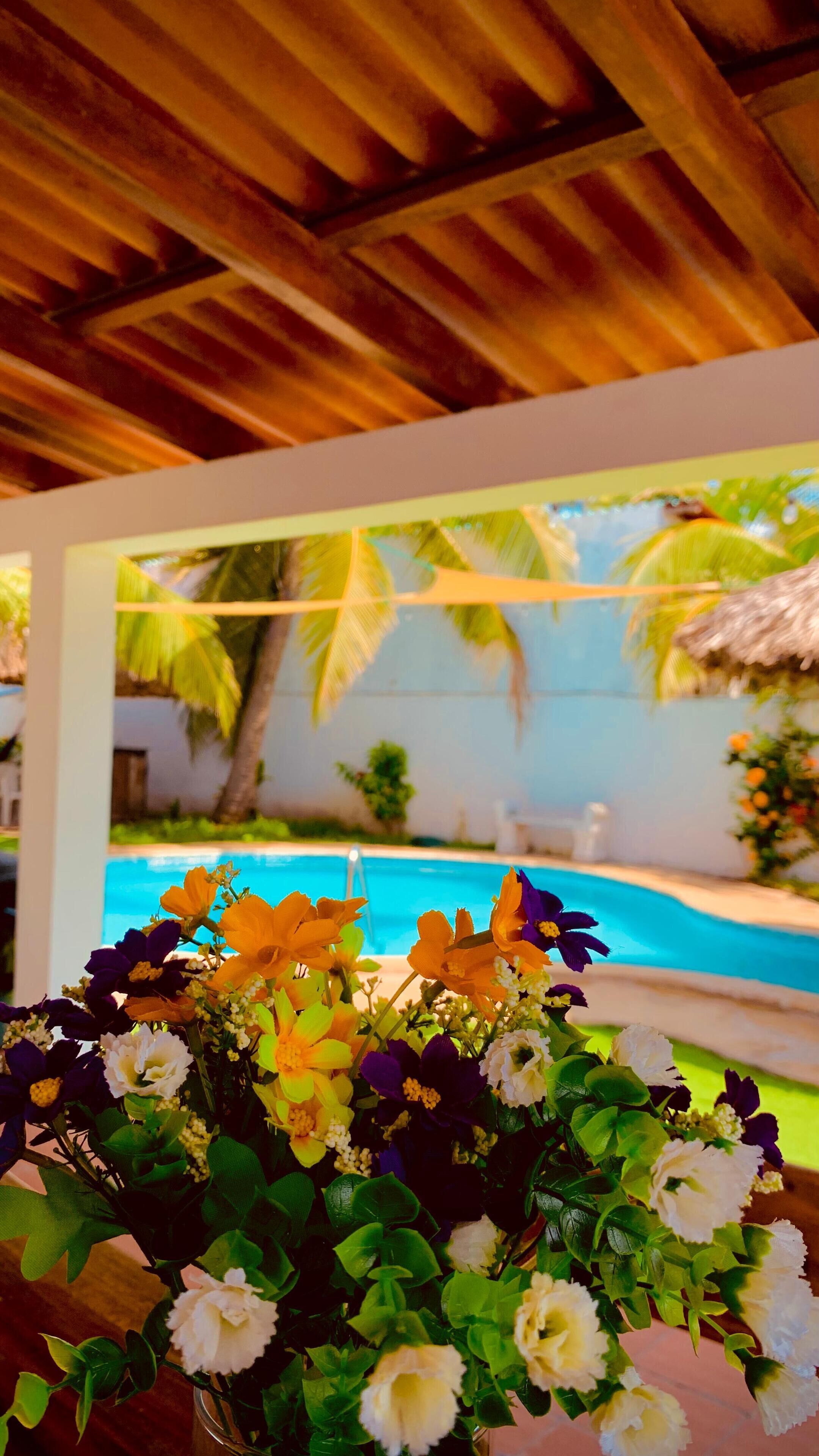 Un espace aménagé au bord de la piscine, avec un plafond en bois, une vue dégagée sur la piscine et une composition florale au premier plan.