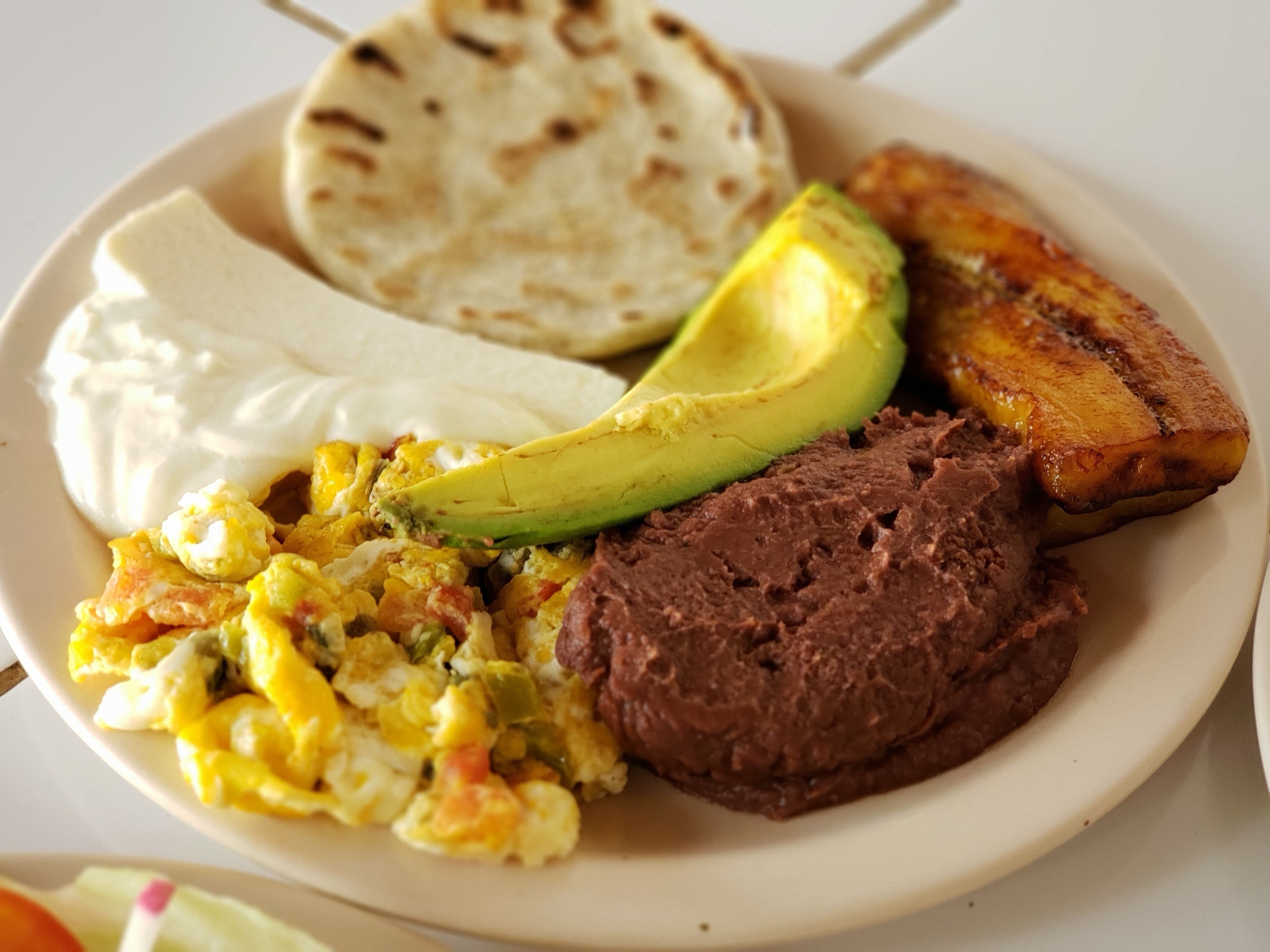 A plate with various foods including avocado, beans, eggs, and plantains.