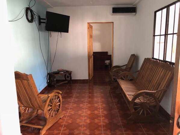 A room with a wooden sofa, two wooden chairs, a small table, and a television mounted on the wall.