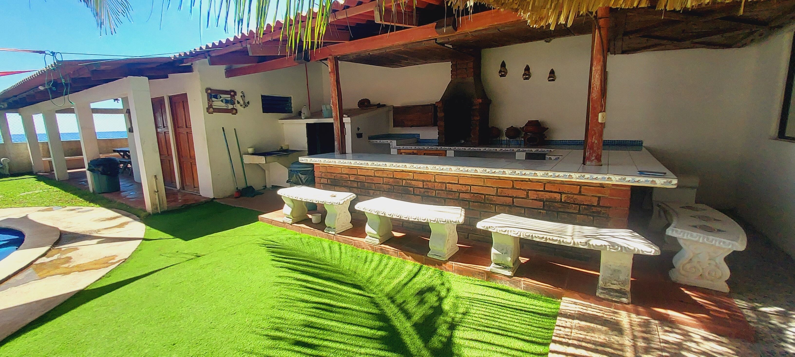 Un patio con barra de ladrillo, taburetes de piedra blanca, una piscina y vista al océano.