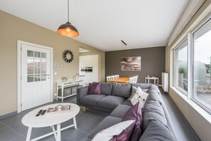 A modern living room with a grey sofa, a white coffee table, and a dining area with a wooden table and chairs. - Koetje Boe (Koksijde)