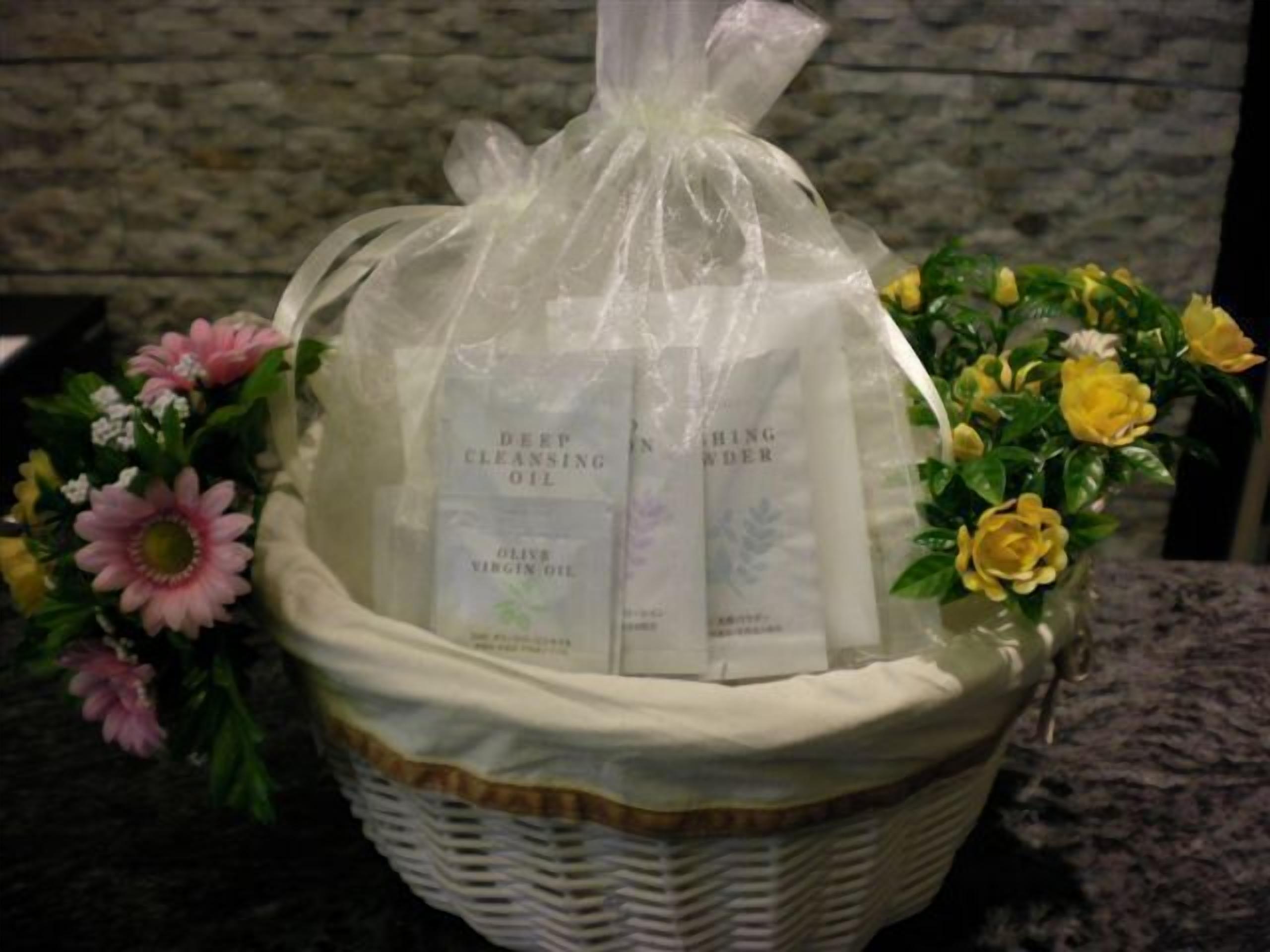 A wicker basket containing two bottles of cleansing oil and a bouquet of flowers.