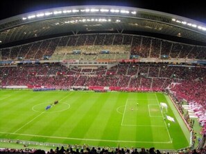 A large stadium with multiple tiers of seating, a well-maintained field, and a crowd of spectators. - Business Hotel Lend (Kawaguchi)