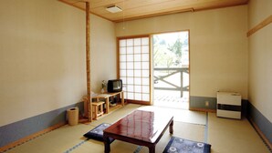Ett traditionellt japanskt rum med tatamimattor på golvet, ett lågt träbord, en tv och skjutdörrar som leder ut till ett utomhusområde.