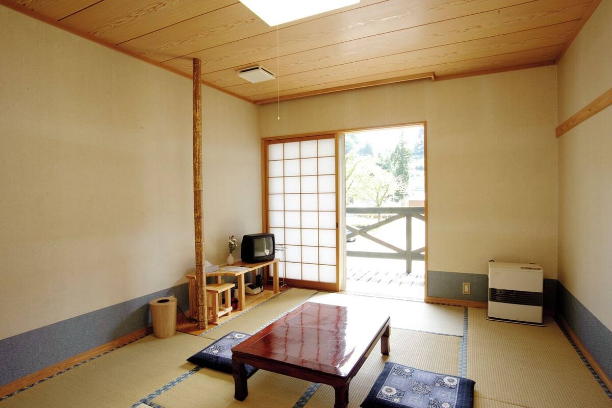A traditional Japanese room with tatami flooring, a low wooden table, a television, and sliding doors leading to an outdoor area.
