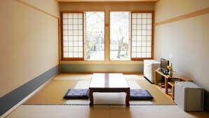 Ett traditionellt japanskt rum med tatamimattor på golvet, ett lågt träbord, ett skrivbord med en dator och en liten luftkonditioneringsanläggning.