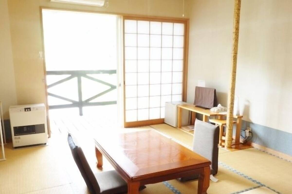A traditional Japanese room with tatami flooring, a low table, a bench, a television, and a sliding door.