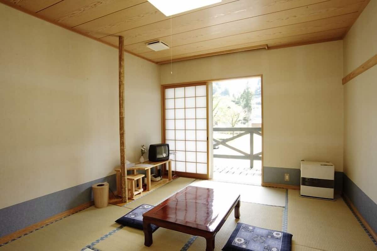A traditional Japanese room with tatami flooring, a tatami mat table, a television, a heater, and a sliding door to a balcony.