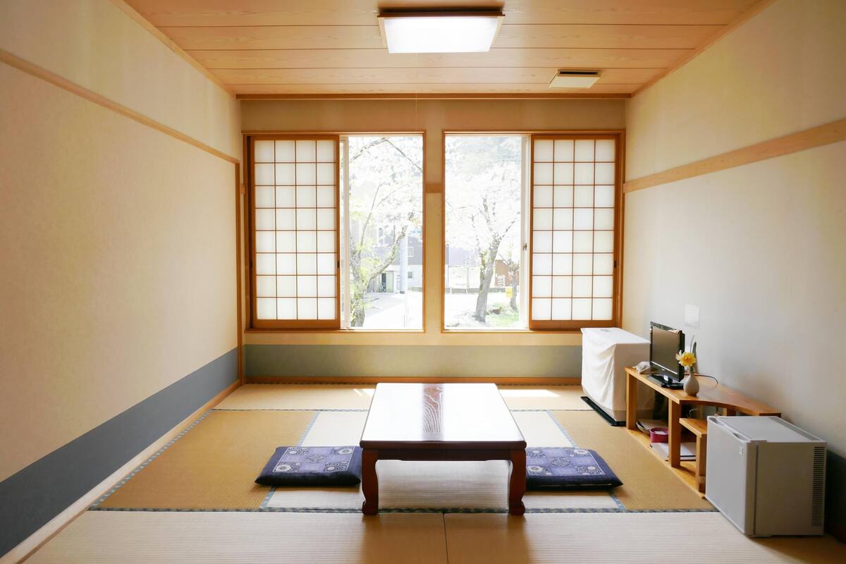 A traditional Japanese room with tatami flooring, a low wooden table, a desk with a computer, and a small air conditioner.