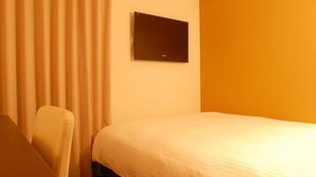 A hotel room with a bed, a chair, a flat-screen TV mounted on the wall, and a window with curtains.