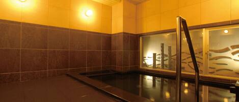 A spa room with a hot tub, tiled walls, and a glass partition with a decorative design.
