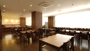 A spacious dining area with multiple wooden tables and chairs, a kitchen in the background, and a bright, well-lit environment. - Ab Hotel Komaki (Komaki)
