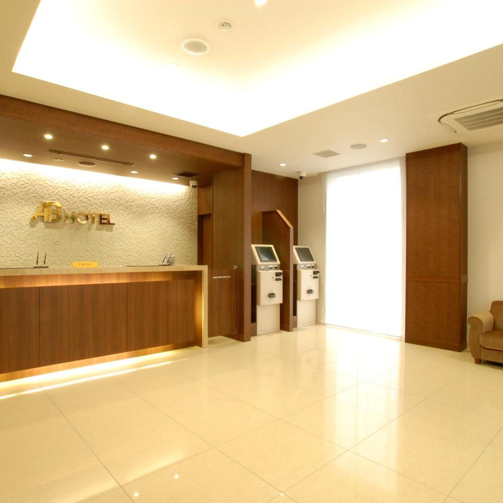 A hotel reception area with a wooden reception desk, a digital check-in kiosk, and a large window.