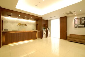 A hotel reception area with a reception desk, a cash register, a digital kiosk, and a sofa. - Ab Hotel Komaki (Komaki)