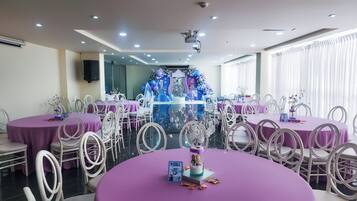 A banquet hall with round tables, white chairs, and purple tablecloths.