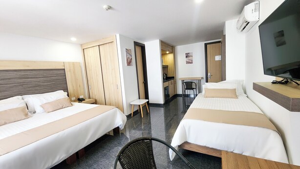 Quarto de hotel com duas camas, uma escrivaninha, uma cadeira, televisão e cozinha compacta.