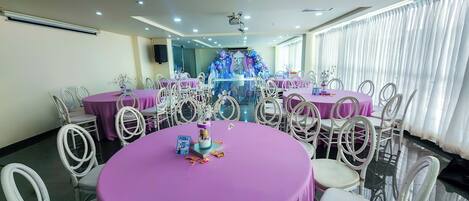 Une salle de conférence avec des tables rondes, des chaises blanches et des nappes violettes.