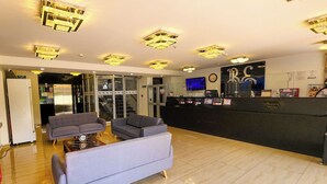 Um saguão de hotel com uma mesa de recepção, dois sofás, um relógio e uma televisão.