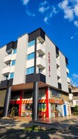 Um hotel com design moderno, exibindo uma placa grande com a palavra 'HOTEL' na fachada, várias varandas e uma área comercial no térreo com vitrines visíveis.