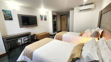 Habitación de hotel con dos camas, un escritorio, una silla, televisión y obras de arte en las paredes.