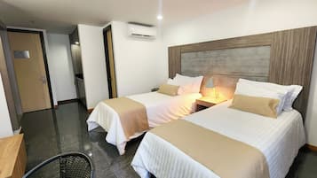 A hotel room with two beds, a wooden headboard, an air conditioning unit, and a small table with a lamp.