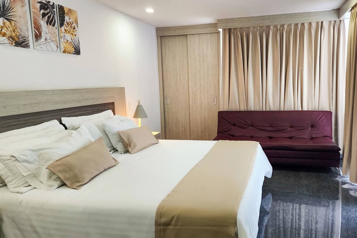 A hotel room with a bed, a sofa, a lamp, and curtains.
