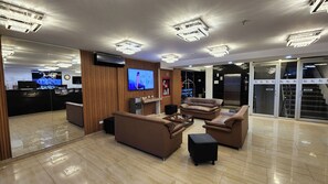 A modern lobby with a reception desk, a flat-screen TV, leather sofas, and a glass elevator. - BE Suites Hotel Cali (Cali)