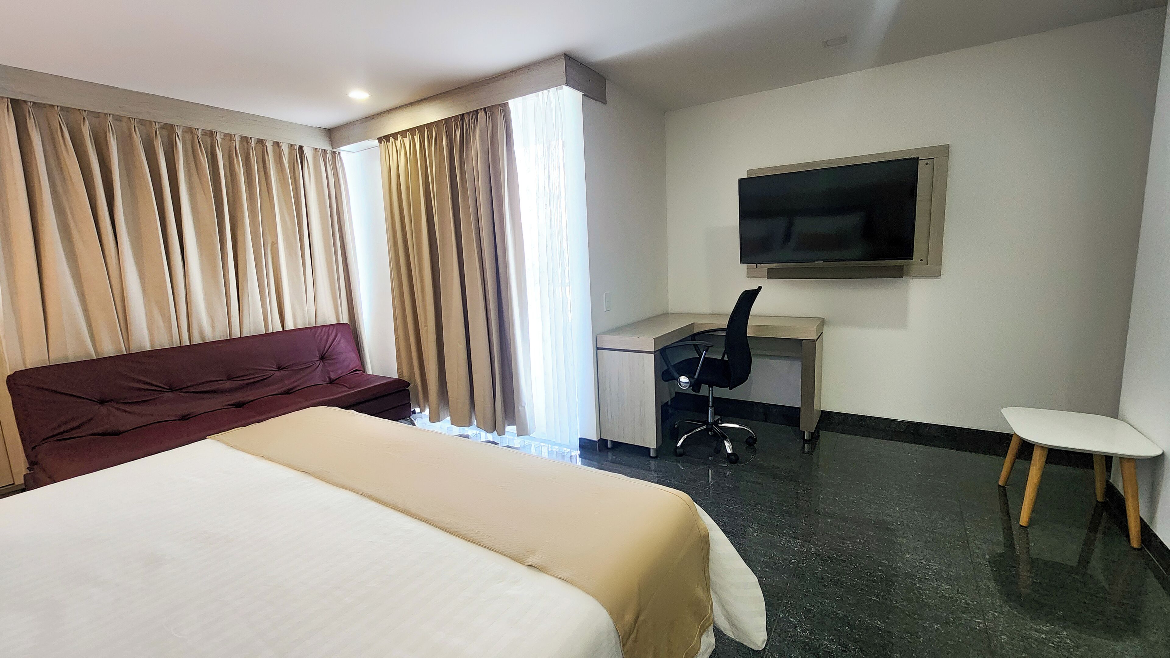 Hotellihuone, jossa on suuri sänky, työpöytä tuolilla, televisio ja verhot.