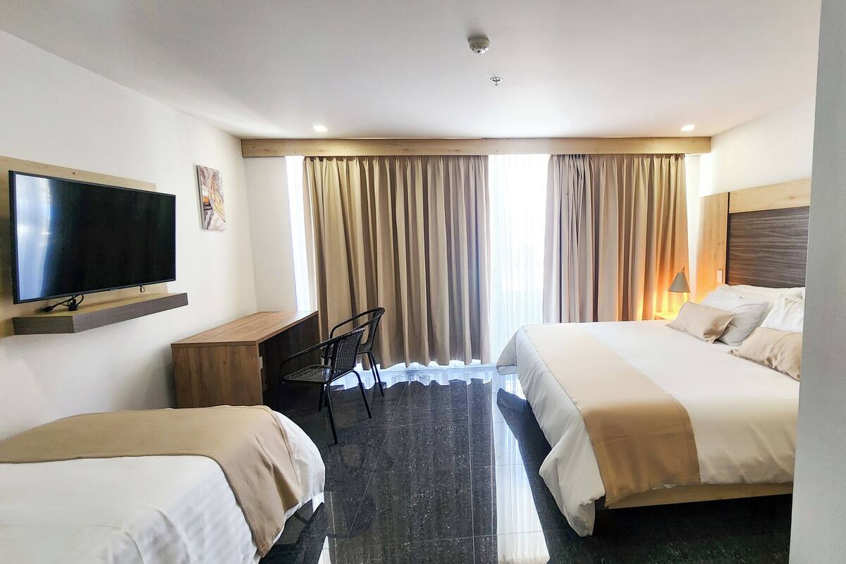 A hotel room with two beds, a desk, a TV, and a window with curtains.