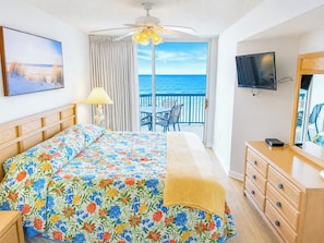 A hotel room with a bed, a TV, a dresser, and a balcony with a view of the sea.